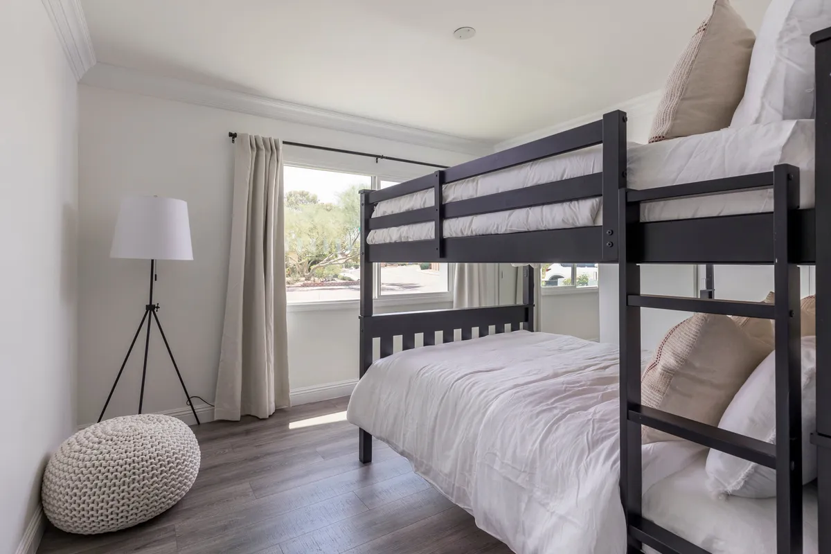 A playful bunk room with a sturdy bunk bed, a large window that fills the room with daylight, a floor lamp, and a cozy pouf. The decor is fun yet comfortable, creating a perfect space for kids or groups to relax and bond.