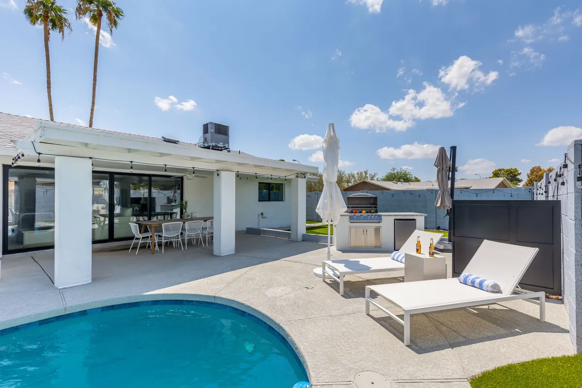 This image features a sparkling swimming pool at the center, with comfortable outdoor seating nearby and a built-in grill station perfect for barbecues. The area is framed by lush landscaping and subtle sunset lighting, evoking a relaxed and inviting vibe for gatherings or quiet lounging.
