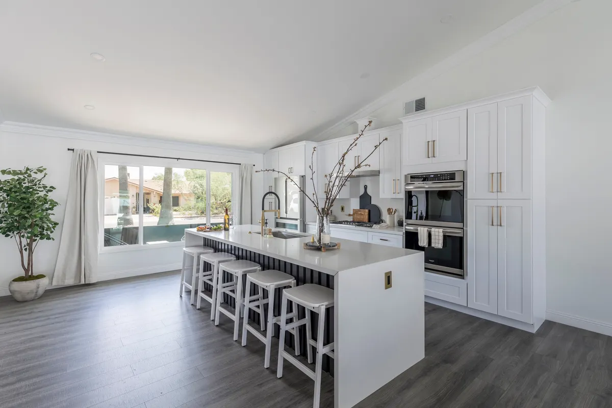 A bright, welcoming kitchen centered around a large kitchen island with bar stools. Modern appliances and natural light create a fresh, inviting space ideal for meal prep or casual breakfasts. The decorative branch centerpiece adds a touch of elegance and warmth, enhancing the kitchen’s hospitality vibe.