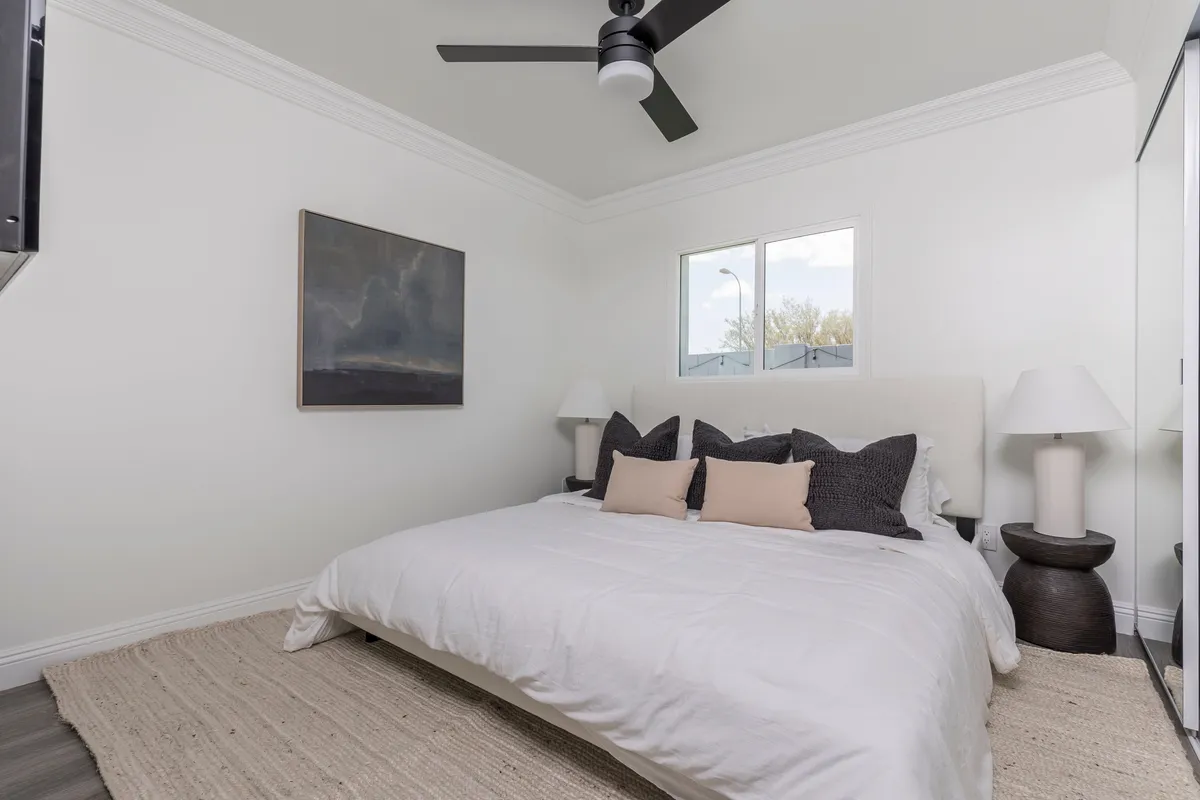 A bright bedroom with a neatly made king bed, stylish artwork above the headboard, matching nightstands, and a window letting in soft natural light. The overall mood is peaceful and inviting, ideal for unwinding after a long day.