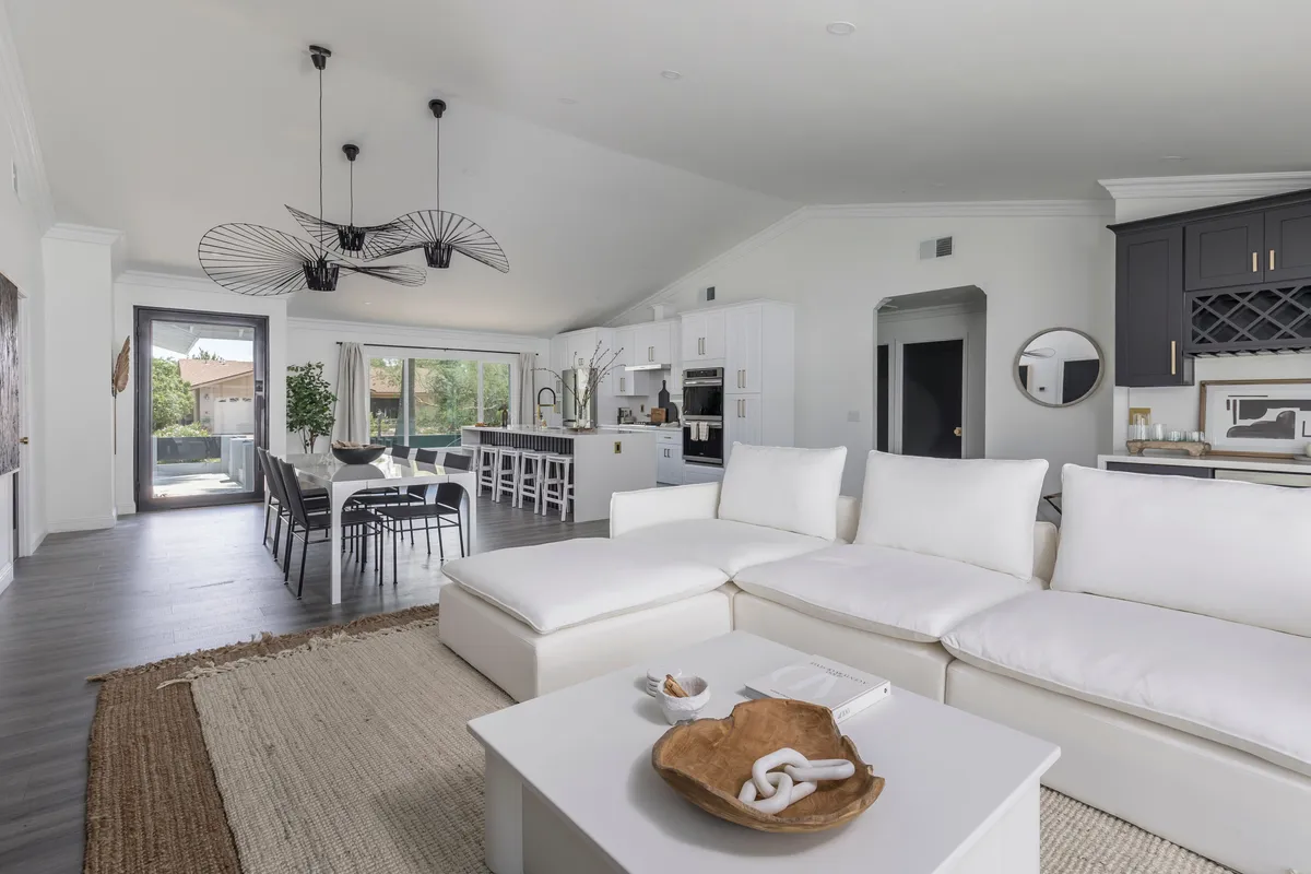 A warm, welcoming interior view featuring a large sectional sofa, a family-style dining table, an open kitchen, and a statement light fixture. The layout is designed for easy gathering, conversation, and shared meals, while the mix of textures and lighting adds to the cozy yet sophisticated ambiance.