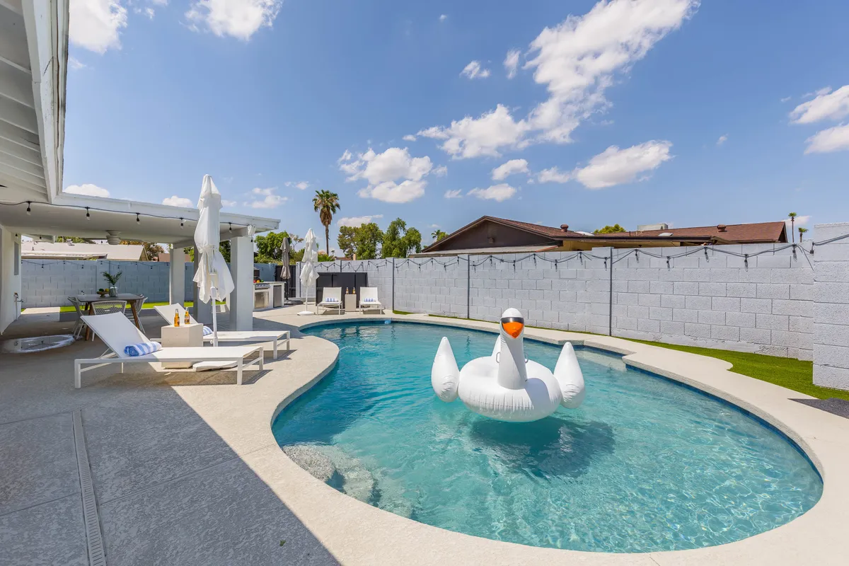 The image showcases a sun-drenched Scottsdale backyard with a sparkling swimming pool, a playful inflatable swan, inviting lounge chairs, and an alfresco dining area. The scene radiates relaxation and fun, hinting at memorable afternoons by the water and lively gatherings under the Arizona sky.
