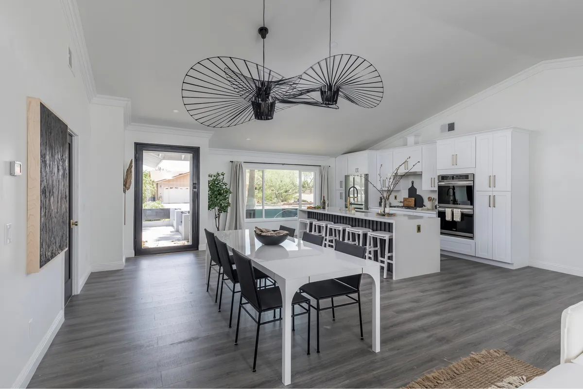 A spacious dining area with a large table perfect for family meals or festive gatherings. The scene includes a modern light fixture and an open kitchen layout in the background, suggesting seamless flow between cooking and dining activities. The setting is designed for interaction, laughter, and shared experiences.