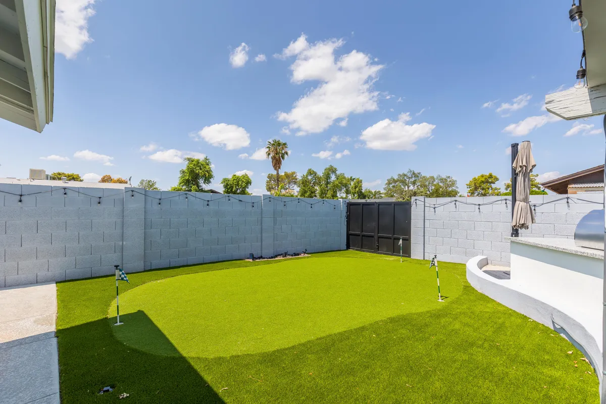 This image displays a cheerful artificial grass lawn enclosed by privacy walls, with cozy outdoor seating and festive string bistro lights overhead. The setup invites family playtime, relaxation, or evening gatherings under the glow of the lights.