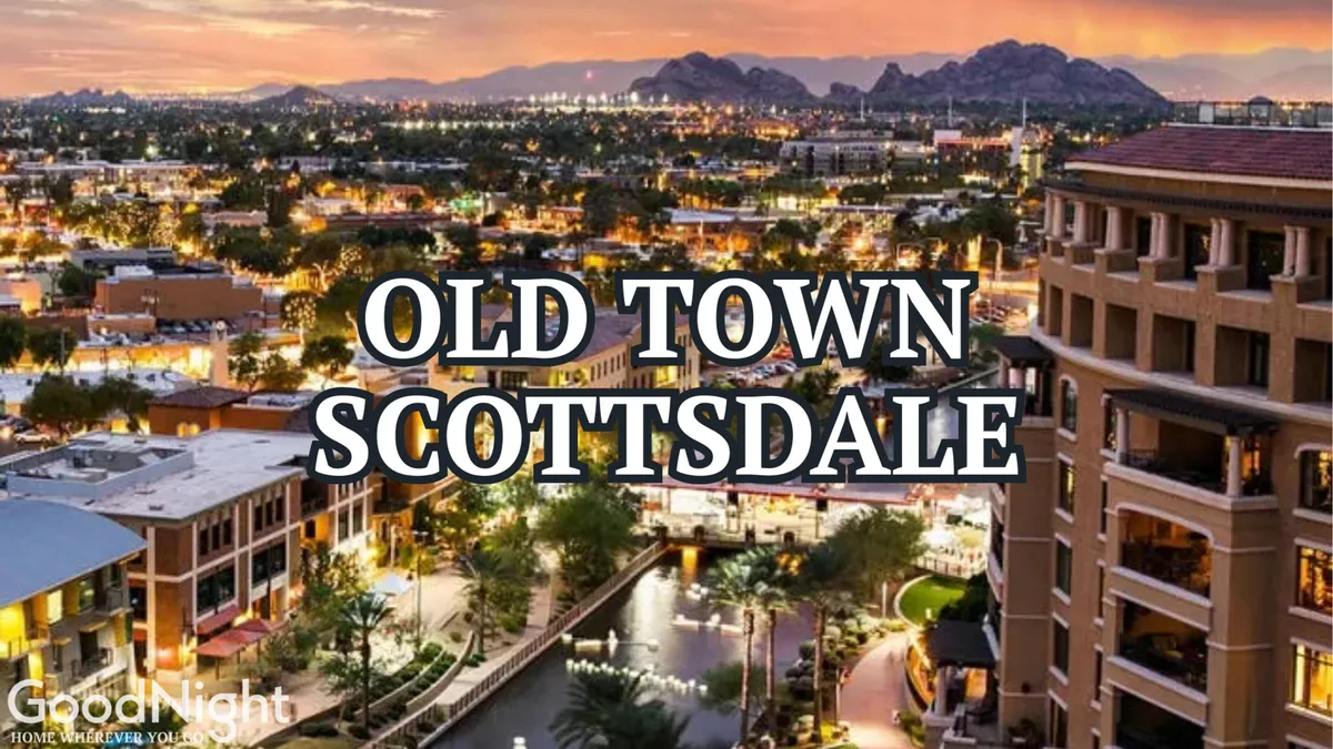 A lively scene of Old Town Scottsdale at sunset, with illuminated buildings reflecting along the waterway and mountains visible in the background. People can be seen dining, shopping, and strolling along the waterfront, capturing the vibrant energy of the area.